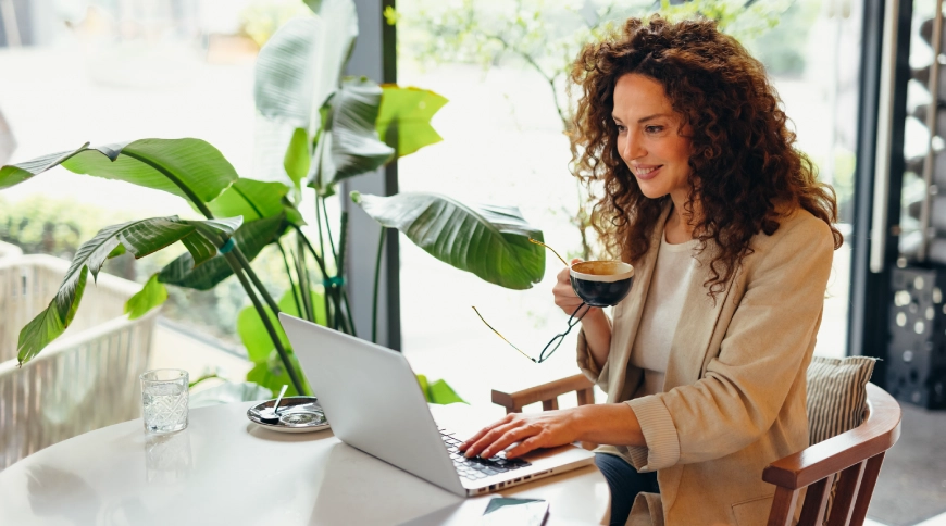 Sieviete gaišā telpā sēž pie galda un skatās portatīvajā datorā