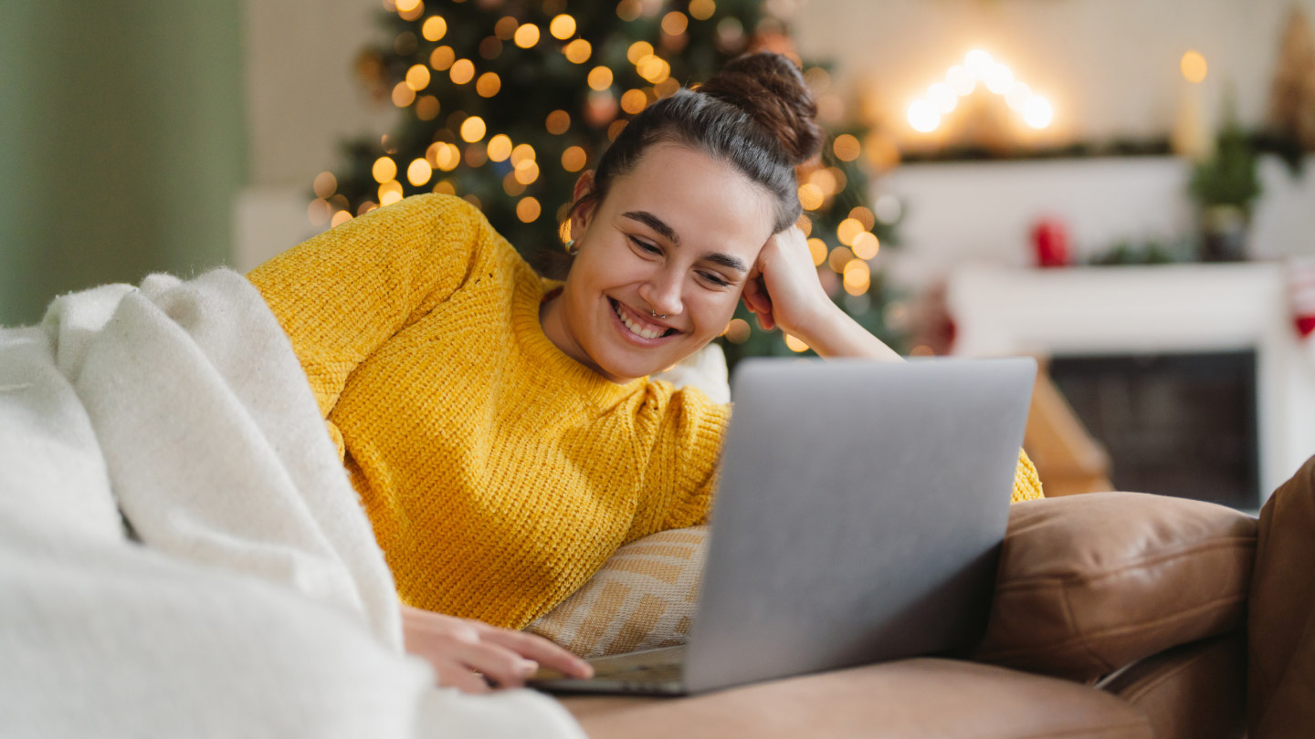 Smaidīga sieviete dīvānā skatās portatīvajā datorā