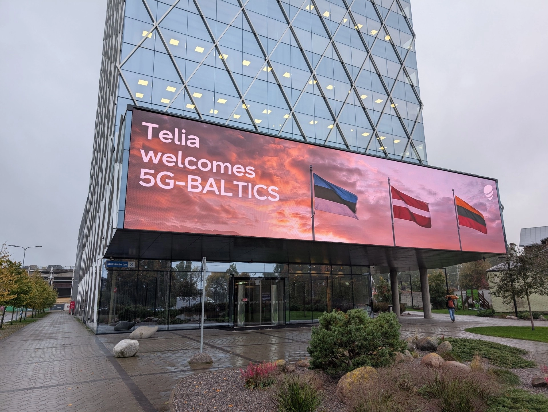 Telia biroja ēka ar ekrānu, kurā redzams uzraksts “Telia welcomes 5G-BALTICS” un Baltijas valstu karogi.