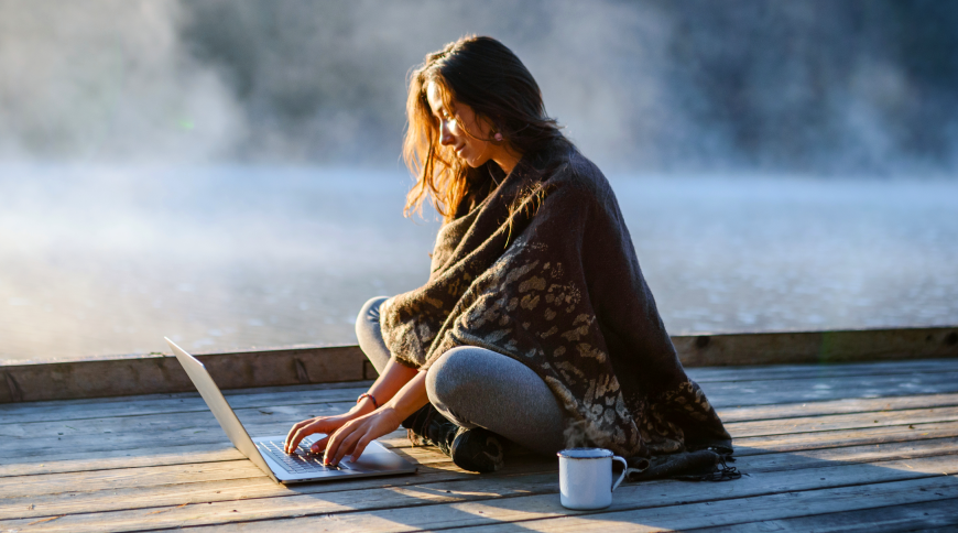 Meitene pie ezera, uz laipas, skatās portatīvajā datorā