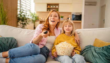 Mamma ar meitu dīvānā skatās TV un ēd popkornu