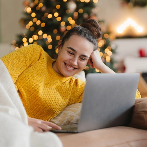 Smaidīga sieviete dīvānā skatās portatīvajā datorā