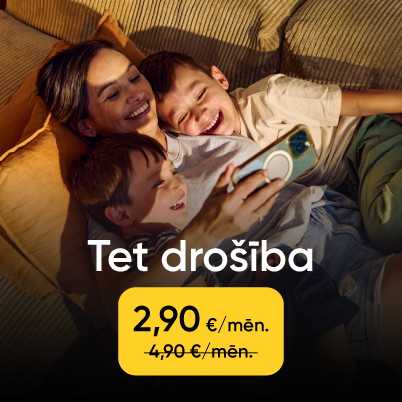 Sieviete ar diviem bērniem guļ uz dīvāna un smaida, skatoties telefonā.
