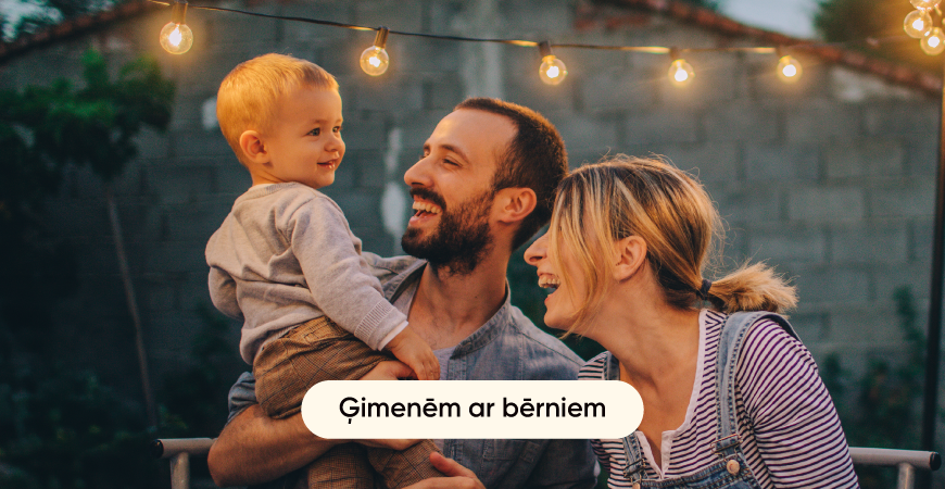 Ģimene ar bērniem sēž pie galda ārā un priecīgi pavada laiku kopā.