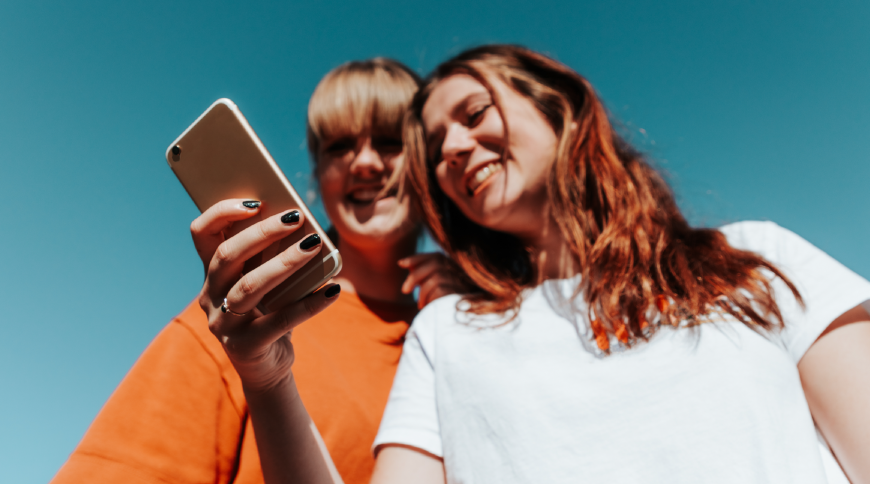 Divas jaunietes skatās telefonā un smaida.