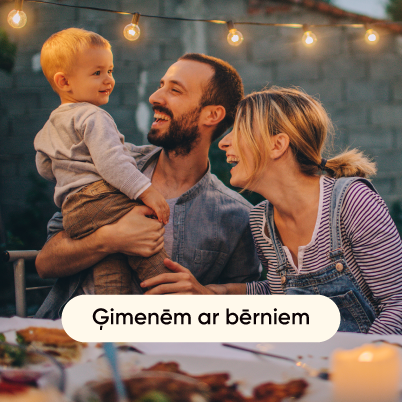 Ģimene ar bērniem sēž pie galda ārā un priecīgi pavada laiku kopā.