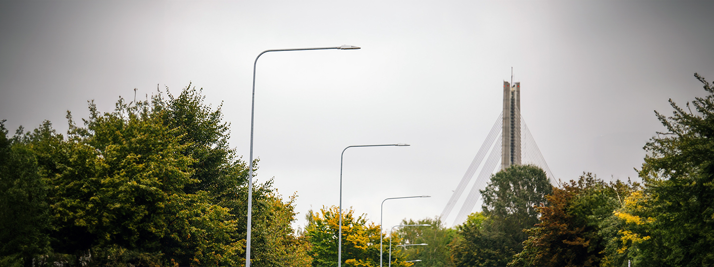 skats uz Vanšu tilta galotni ar gaismas stabiem un kokiem priekšplānā