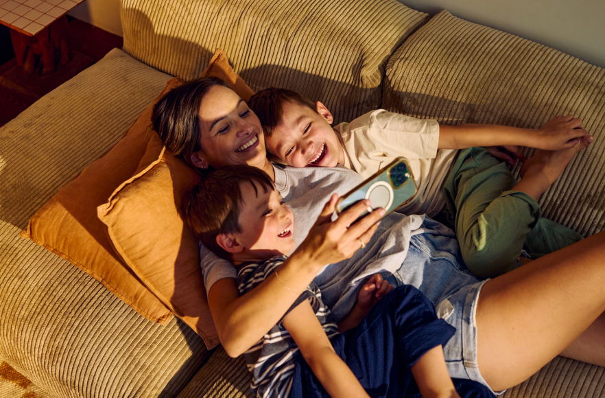 Vīrietis sēž krēslā ar planšetdatoru rokās un bērns pārliecies pāri krēsla malai skatās planšetē