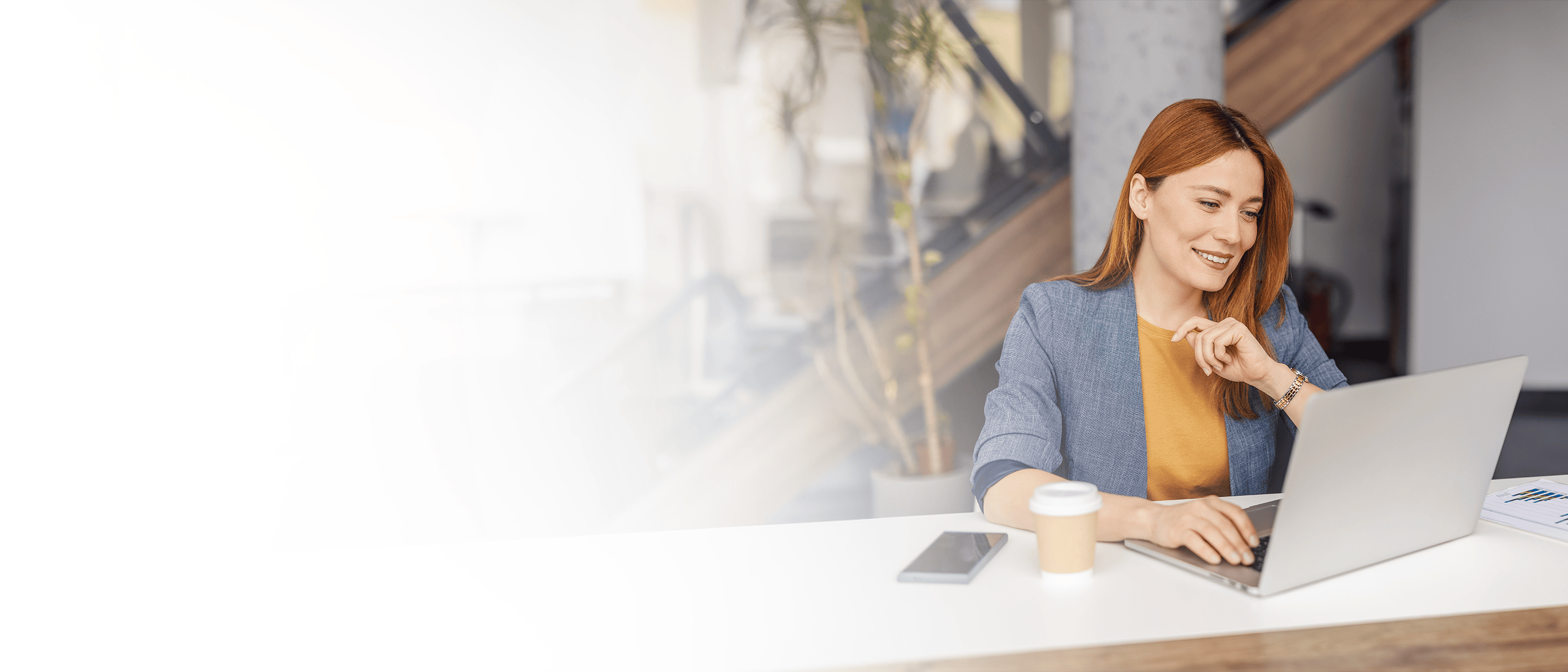 sieviete uzvalkā sēž pie datorgalda un smaida