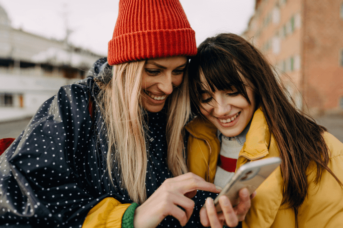 divas sievietes skatās telefonā un smejās