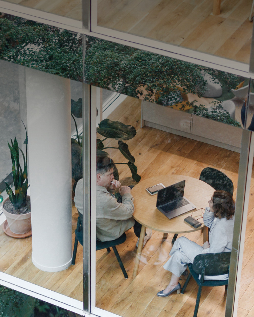 Skats no augšas uz diviem cilvēkiem pie apaļa galda ar klēpjdatoru.