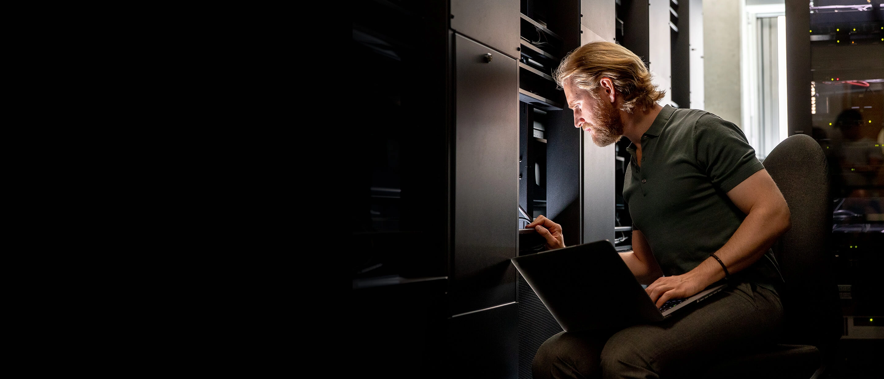 Vīrietis ar klēpjdatoru strādā serveru telpā, pārbauda vai labo aparatūru vienā no serveru skapjiem.