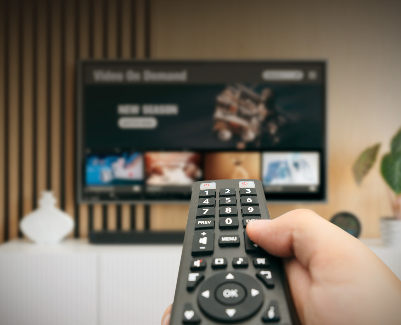 Roka ar TV pulti vērsta pret viedtelevizoru ar straumēšanas izvēlni.