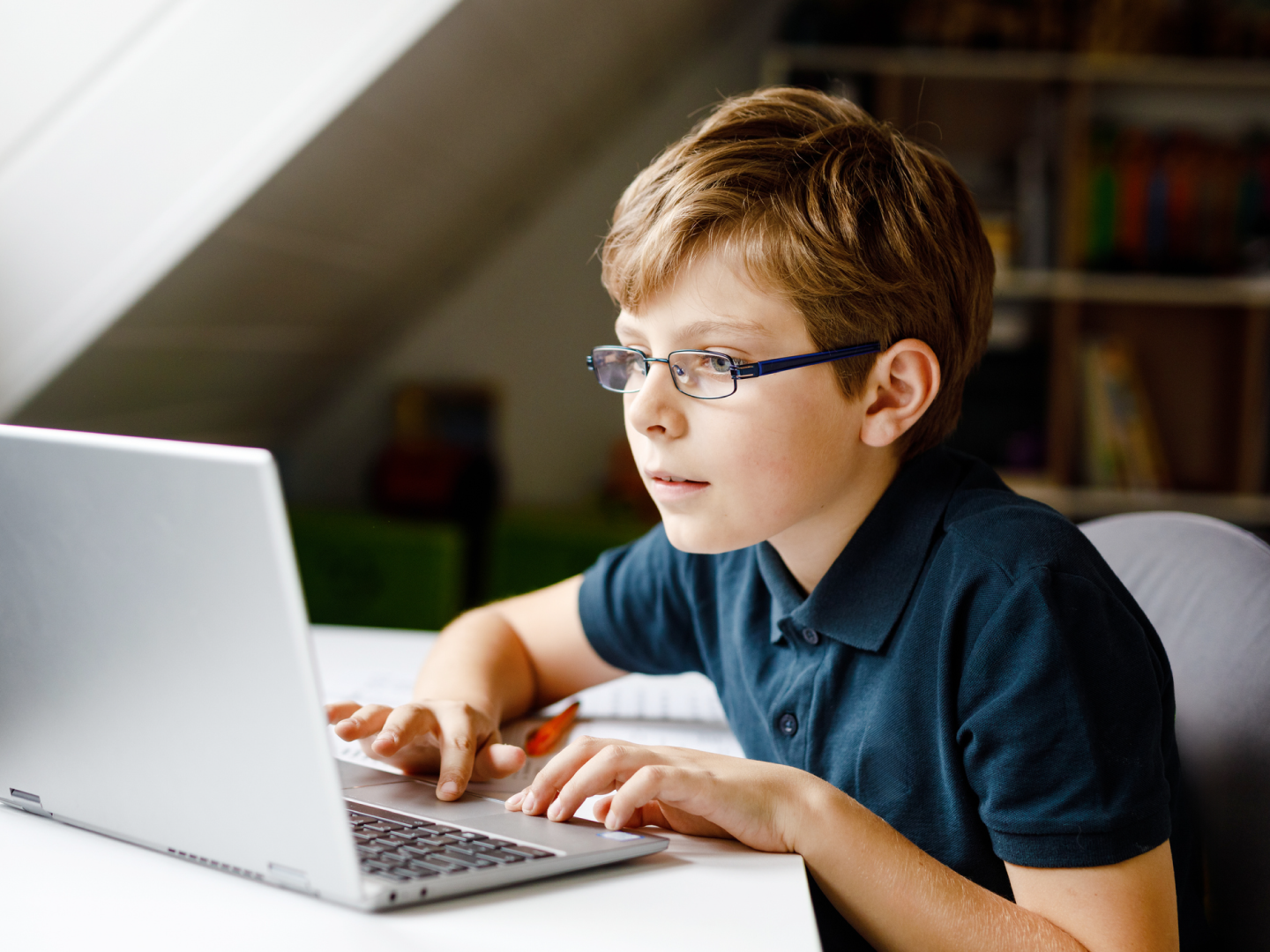 Bērns mācās tiešsaistē: sēž pie klēpjdatora istabā un raksta.