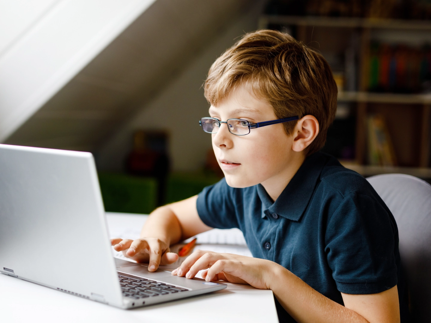 Bērns mācās tiešsaistē: sēž pie klēpjdatora istabā un raksta.