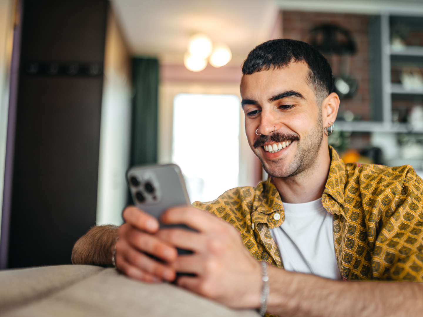 Sieviete atslābusi dīvānā smaidot skatās planšetē mājās.